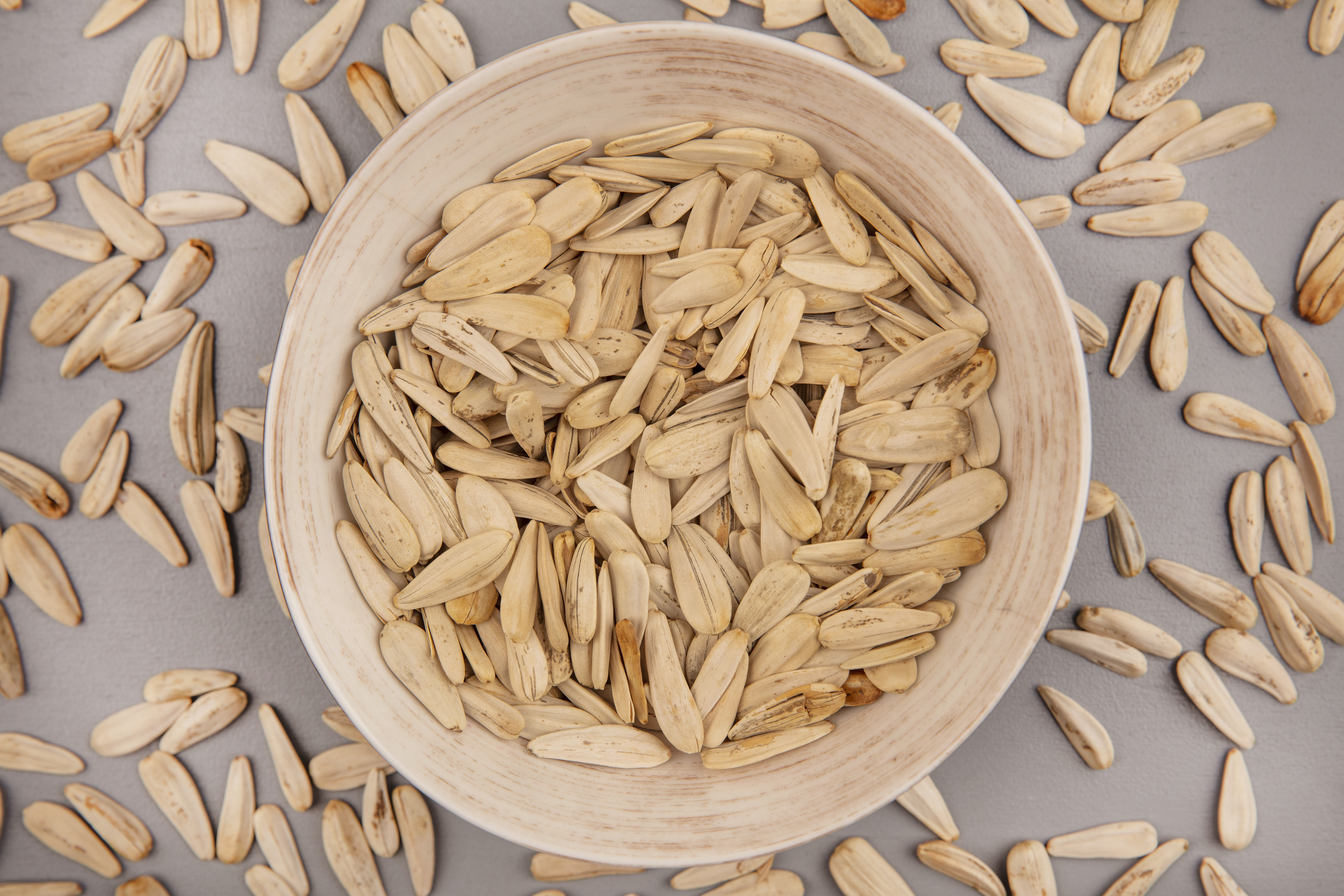 top view of tasty and salty white sunflower seeds on a bowl with sunflower seeds isolated on a grey background
